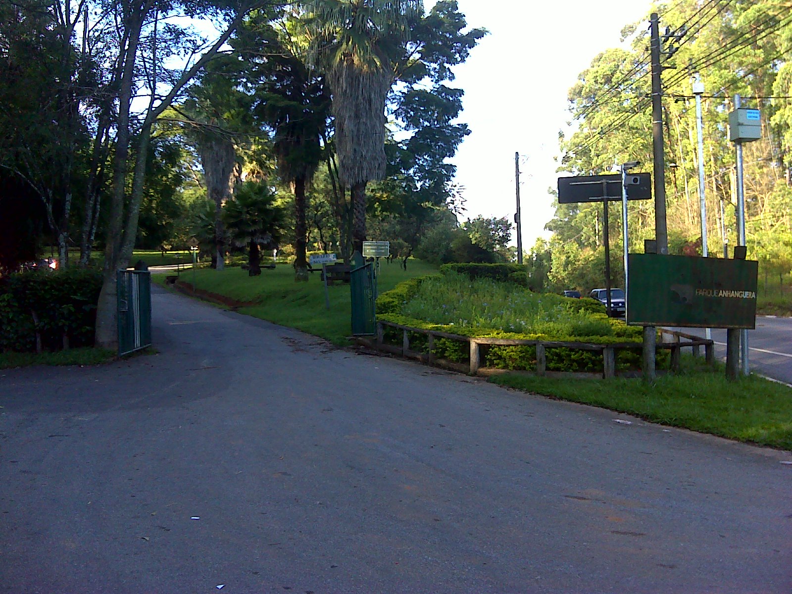 Entrada do Parque Anhanguera, com portão, canteiro e placa à beira da via